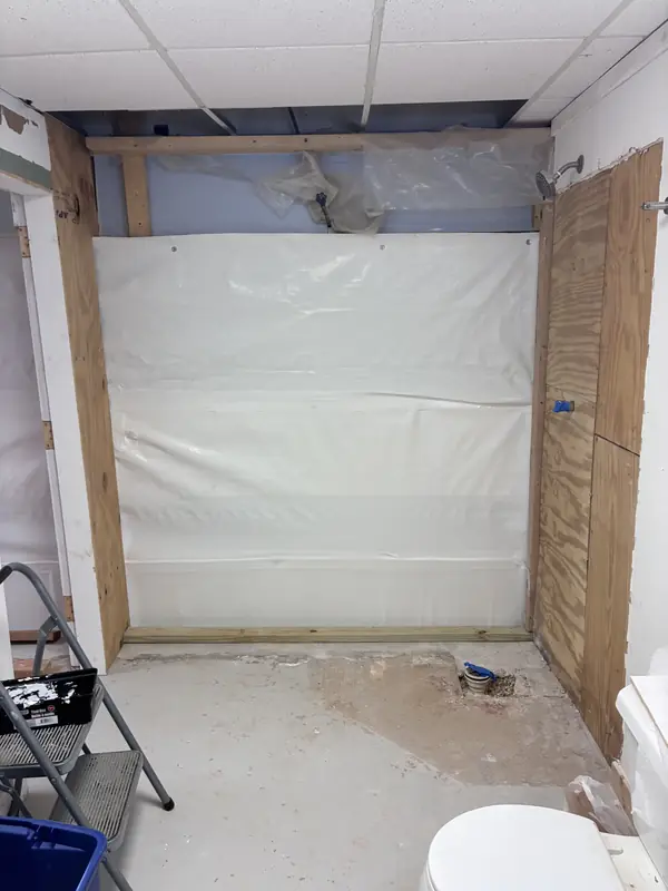 Bathroom work area with an opened wall, exposed wood panels and plastic sheeting