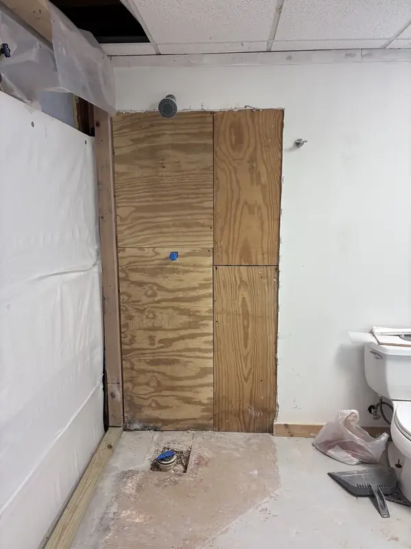 Exposed wood wall panels next to plastic sheeting in a bathroom work area