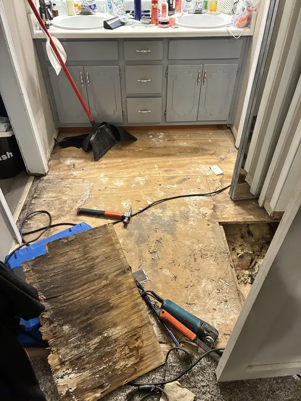 Bathroom floor opened around a vanity with removed material and tools nearby