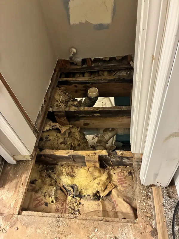 Removed bathroom flooring revealing joists, insulation and plumbing below