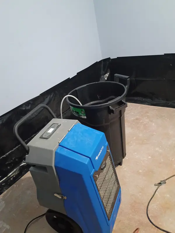 Blue dehumidifier with a collection tub and hose in a room with exposed subfloor