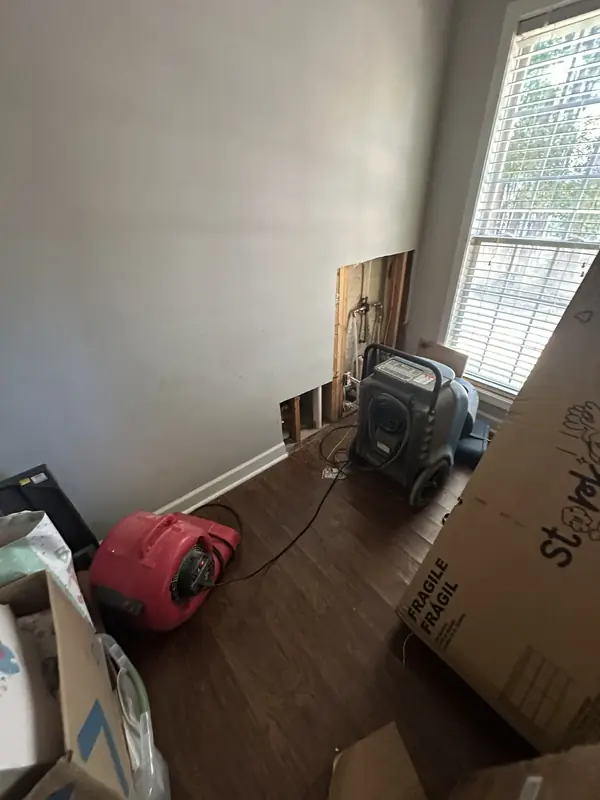 Air movers beside an opened lower wall in a room with wood flooring